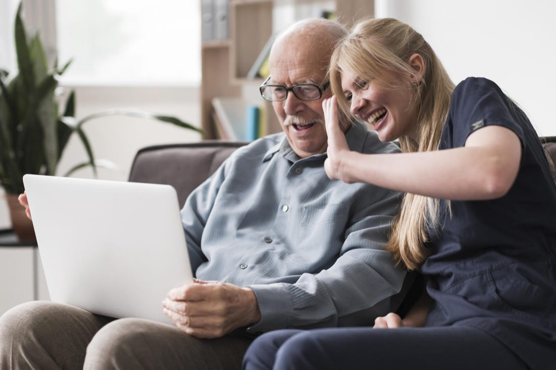 Nurse with a senior citizen in front of a laptop waving